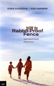 portada de la novela «Follow the Rabbit-Proof Fence», donde tres chicas aborígenes australianas cruzan un desierto bajo un cielo azul pálido