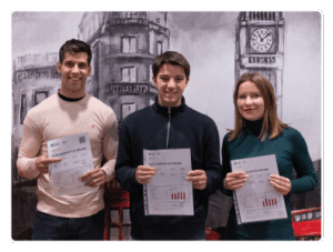 Tres estudiantes felices que han aprobado el examen Aptis posan mirando a cámara con sus certificados en la mano en nuestra academia de inglés en Madrid