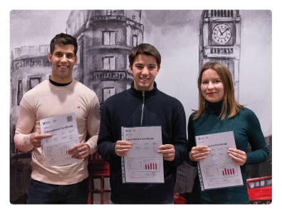 Tres estudiantes felices que han aprobado el examen Aptis posan mirando a cámara con sus certificados en la mano