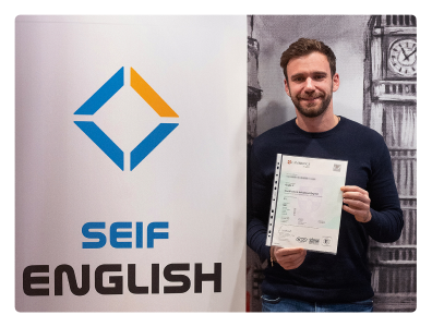 Estudiante sonriente en las modernas instalaciones de la academia en Gran Vía 50, mirando a cámara y sosteniendo su certificado que demuestra haber aprobado el examen Cambridge Advanced.