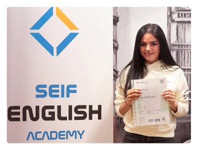 Estudiante sonriente en las modernas instalaciones de la academia en Gran Vía 50, mirando a cámara y sosteniendo su certificado que demuestra haber aprobado el examen Cambridge Proficiency