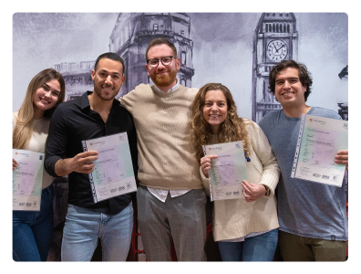 Profesor nativo sonriente con sus estudiantes en las modernas instalaciones de la academia en Gran Vía 50, mirando a cámara y sosteniendo sus certificados que demuestran haber aprobado un examen de Cambridge