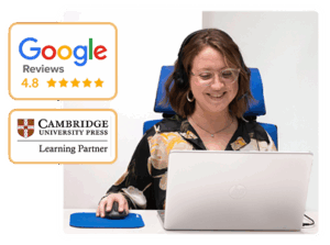 Una sonriente profesora sentada en nuestra academia frente a un ordenador imparte preparación de exámenes Cambridge en Madrid online.