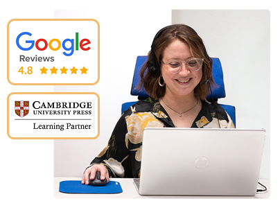 Una sonriente profesora sentada en nuestra academia frente a un ordenador imparte preparación de exámenes Cambridge en Madrid online.